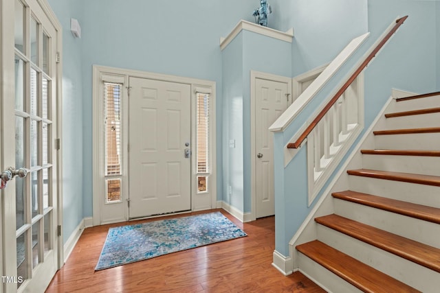 foyer entrance with stairway, wood finished floors, baseboards, and a towering ceiling