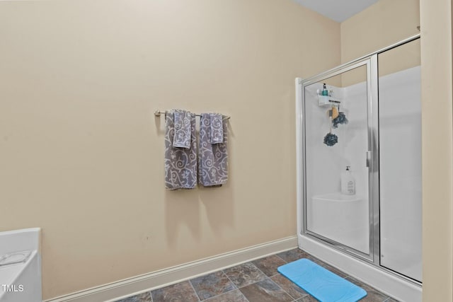 bathroom with a stall shower, stone finish flooring, and baseboards