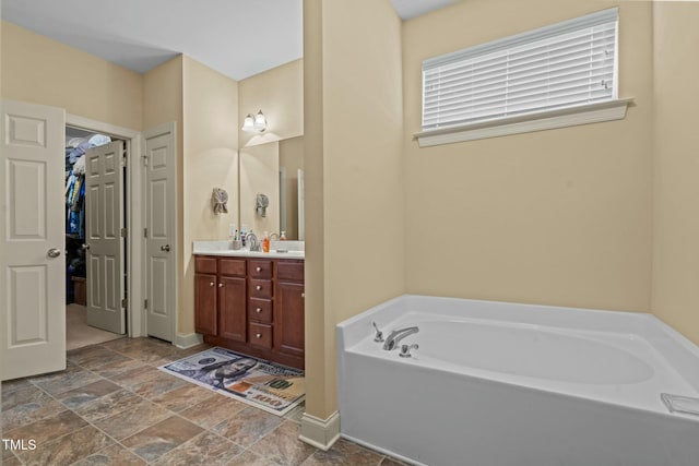 bathroom featuring a bath, double vanity, a walk in closet, and stone finish flooring