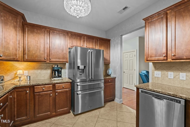 kitchen featuring appliances with stainless steel finishes, backsplash, light tile patterned floors, light stone counters, and a chandelier