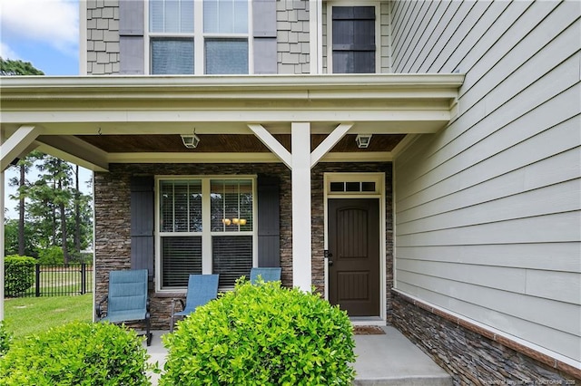 entrance to property featuring fence, a porch, and stone siding