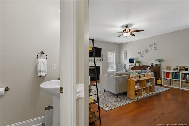 living area featuring ceiling fan, a glass covered fireplace, and wood finished floors