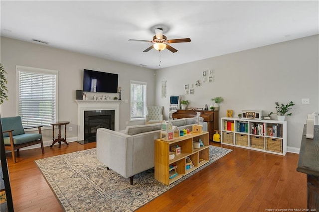 living area with a ceiling fan, wood finished floors, a fireplace with flush hearth, and baseboards