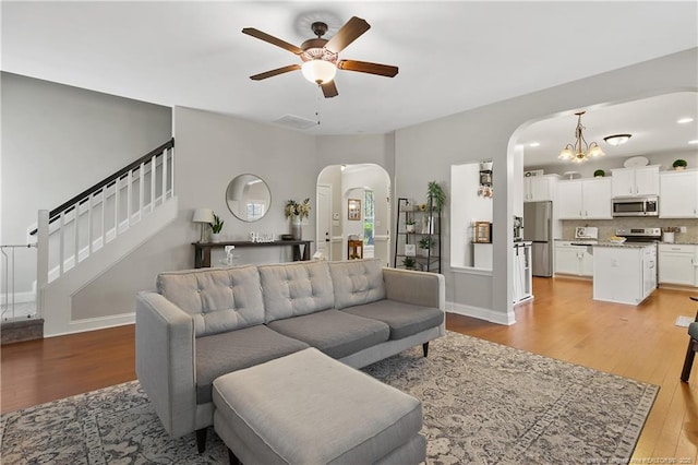 living room with arched walkways, ceiling fan, light wood-type flooring, and stairway