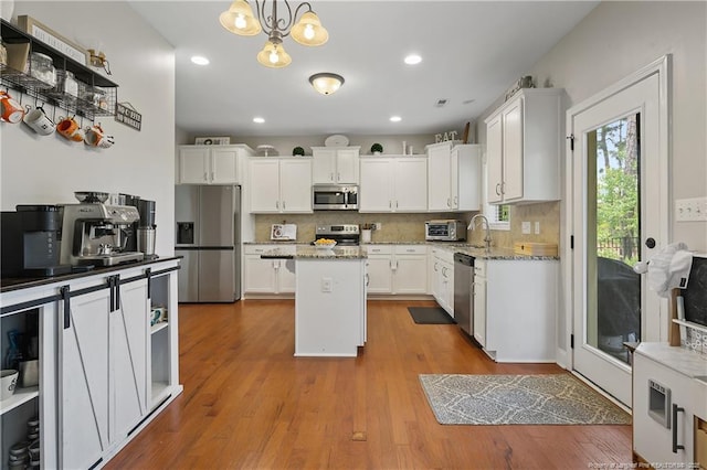 kitchen with appliances with stainless steel finishes, a kitchen island, white cabinetry, backsplash, and a sink