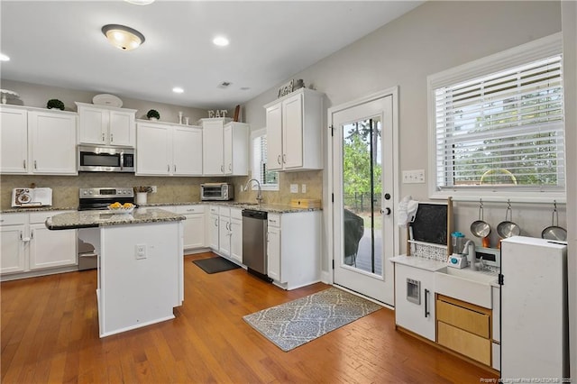 kitchen with stainless steel appliances, tasteful backsplash, white cabinetry, hardwood / wood-style flooring, and a center island