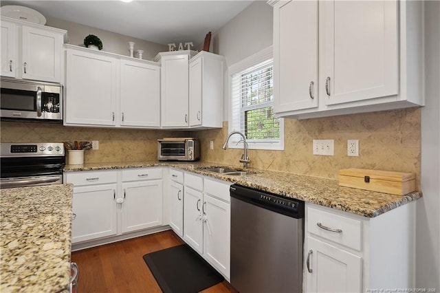 kitchen with stainless steel appliances, a sink, white cabinets, light stone countertops, and dark wood-style flooring