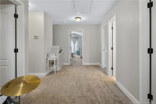 hallway featuring attic access, light colored carpet, baseboards, and an upstairs landing