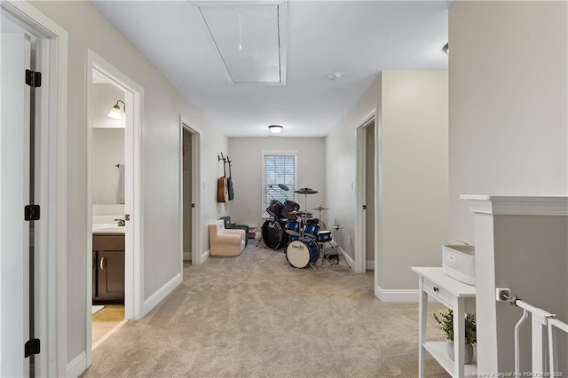 hall featuring attic access, light carpet, baseboards, and a sink