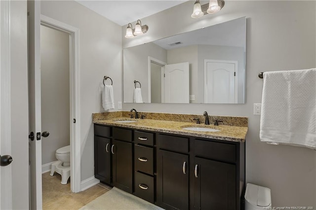 bathroom with toilet, double vanity, tile patterned floors, and baseboards