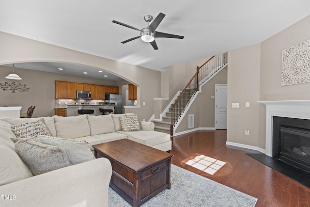 living area with arched walkways, dark wood finished floors, stairs, a ceiling fan, and visible vents