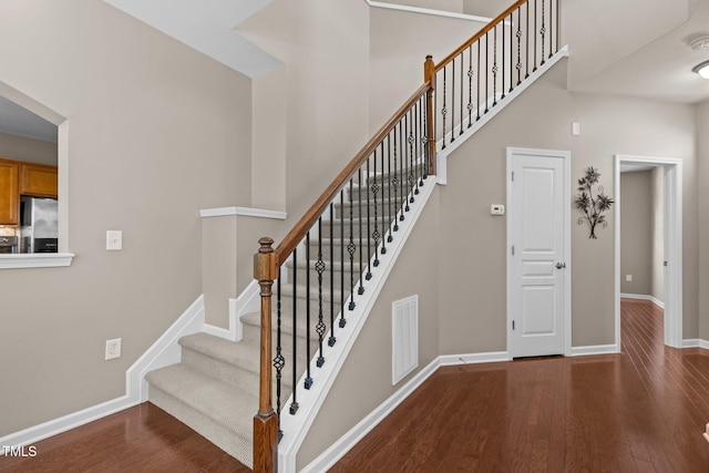 staircase featuring baseboards, visible vents, wood finished floors, and a towering ceiling