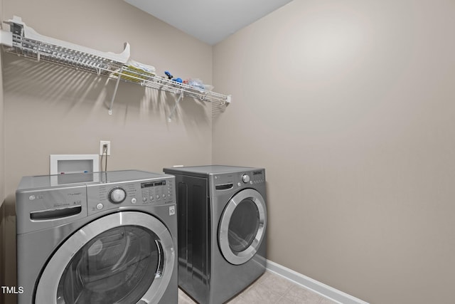 clothes washing area featuring light tile patterned floors, laundry area, washing machine and dryer, and baseboards
