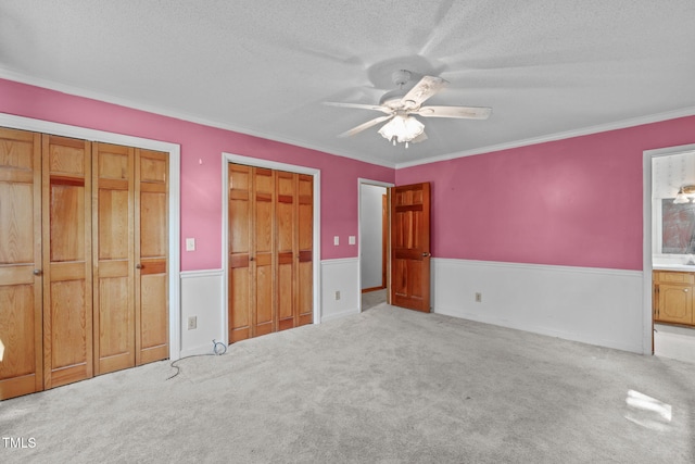 unfurnished bedroom featuring a textured ceiling, a wainscoted wall, two closets, ornamental molding, and carpet