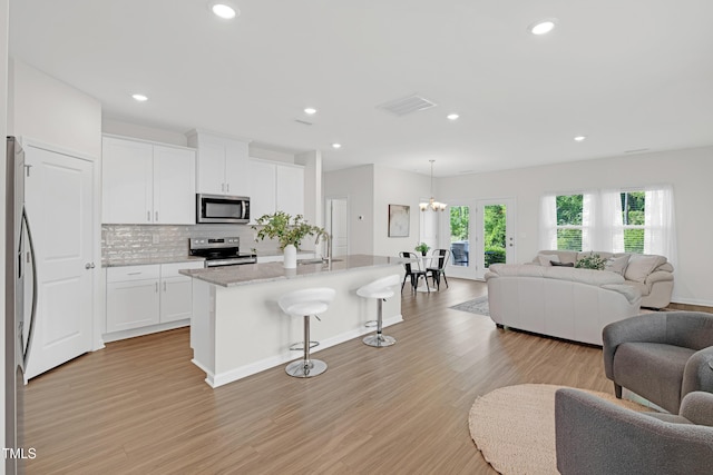 kitchen with visible vents, decorative backsplash, open floor plan, a kitchen bar, and stainless steel appliances