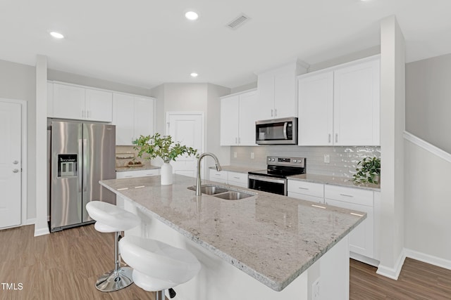 kitchen with baseboards, tasteful backsplash, a sink, light wood-style flooring, and stainless steel appliances