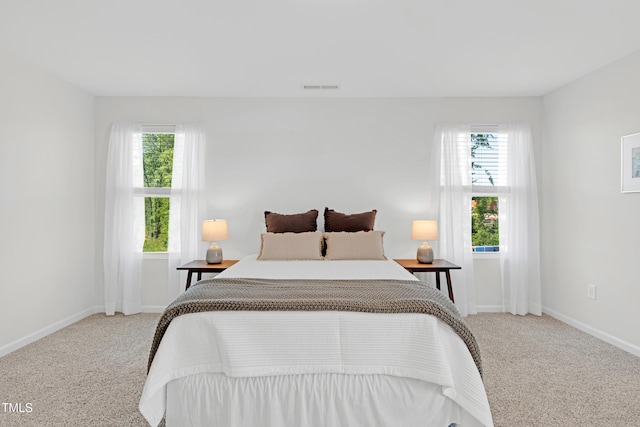bedroom featuring baseboards, multiple windows, visible vents, and light colored carpet