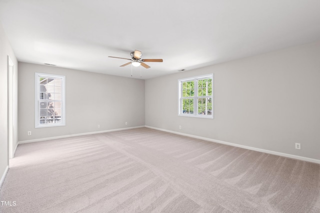 empty room featuring ceiling fan, a wealth of natural light, and light carpet