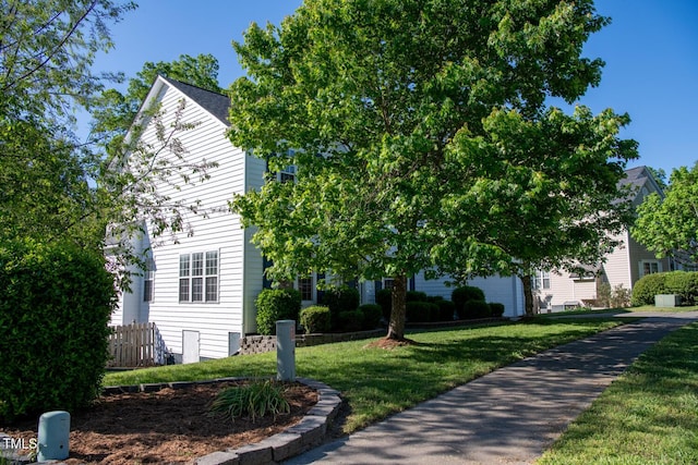 view of property hidden behind natural elements with a front lawn and fence