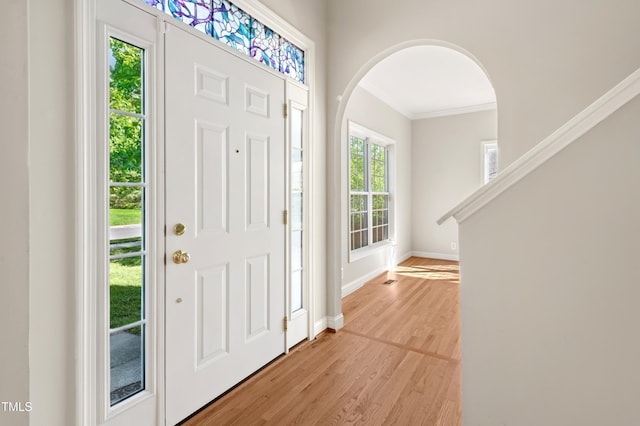 foyer entrance featuring light wood-style floors, arched walkways, ornamental molding, and baseboards