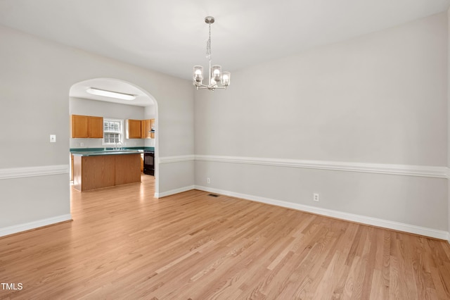 unfurnished room featuring arched walkways, a sink, baseboards, a notable chandelier, and light wood-style floors