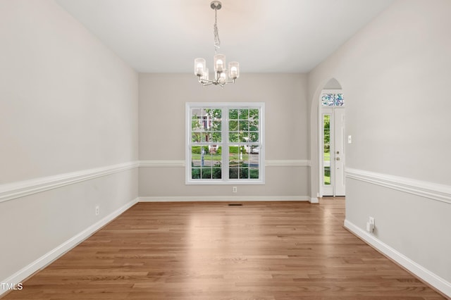 unfurnished dining area featuring arched walkways, baseboards, a notable chandelier, and wood finished floors