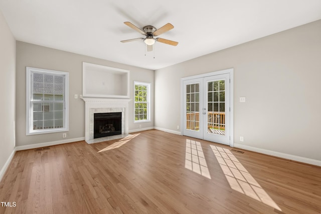 unfurnished living room with wood finished floors, baseboards, a high end fireplace, french doors, and a ceiling fan