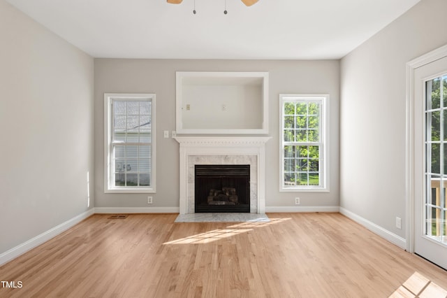unfurnished living room with a high end fireplace, baseboards, a ceiling fan, and wood finished floors