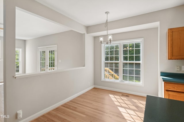 unfurnished dining area with baseboards, light wood finished floors, a chandelier, and visible vents