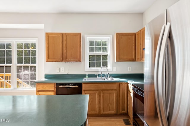 kitchen with visible vents, brown cabinets, a sink, black appliances, and light wood finished floors