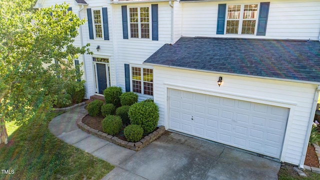 traditional home with a garage, a shingled roof, and driveway