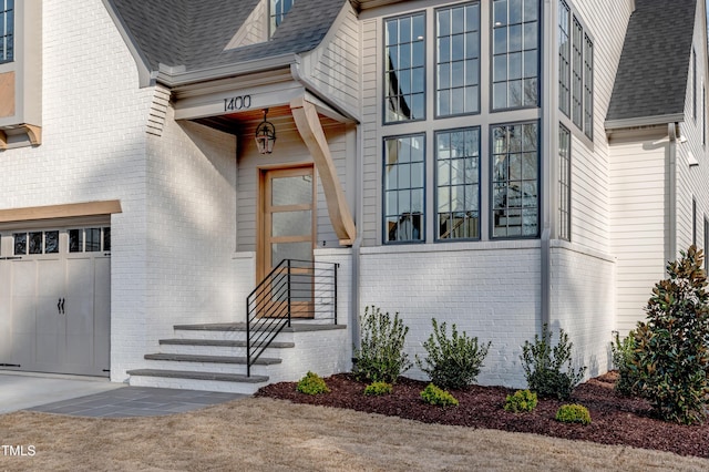 entrance to property with a shingled roof, an attached garage, and brick siding