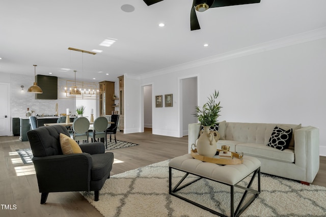 living area with baseboards, light wood-type flooring, ornamental molding, and ceiling fan with notable chandelier
