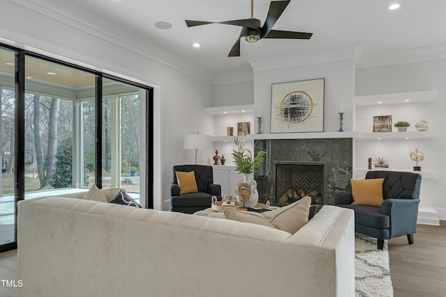 living area with ornamental molding, recessed lighting, a premium fireplace, and wood finished floors