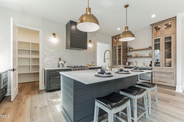 kitchen featuring wall chimney range hood, beverage cooler, light wood-style floors, light countertops, and backsplash