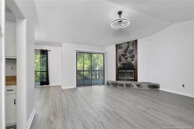 unfurnished living room with lofted ceiling, wood finished floors, a wealth of natural light, and a fireplace
