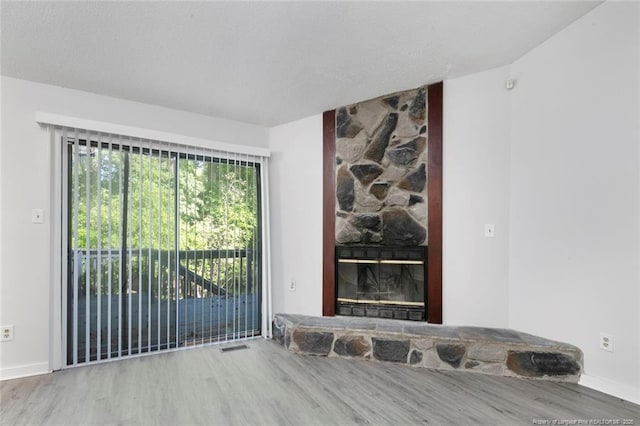interior space with baseboards, a stone fireplace, and wood finished floors