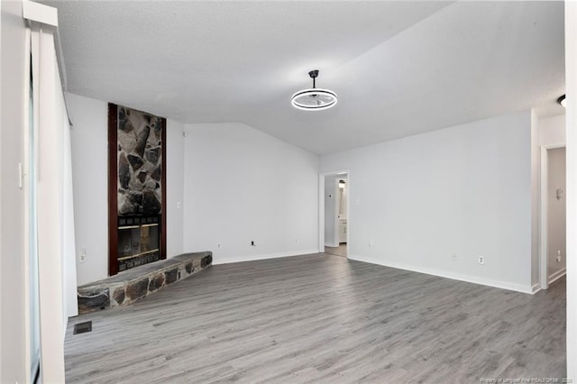 spare room with visible vents, a fireplace, vaulted ceiling, wood finished floors, and baseboards