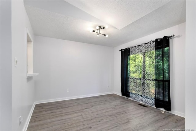 unfurnished room with wood finished floors, baseboards, a textured ceiling, and visible vents