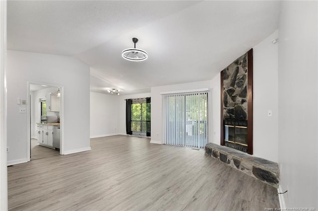 unfurnished living room featuring light wood-style floors, baseboards, a stone fireplace, and lofted ceiling