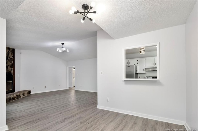 unfurnished living room with baseboards, a textured ceiling, lofted ceiling, and wood finished floors