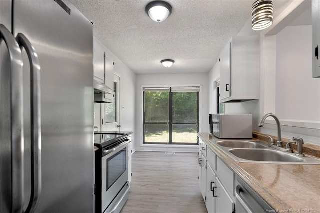 kitchen with white cabinets, appliances with stainless steel finishes, a sink, a textured ceiling, and wall chimney exhaust hood