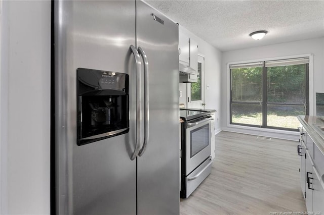 kitchen featuring white cabinets, wall chimney range hood, appliances with stainless steel finishes, light wood finished floors, and a textured ceiling