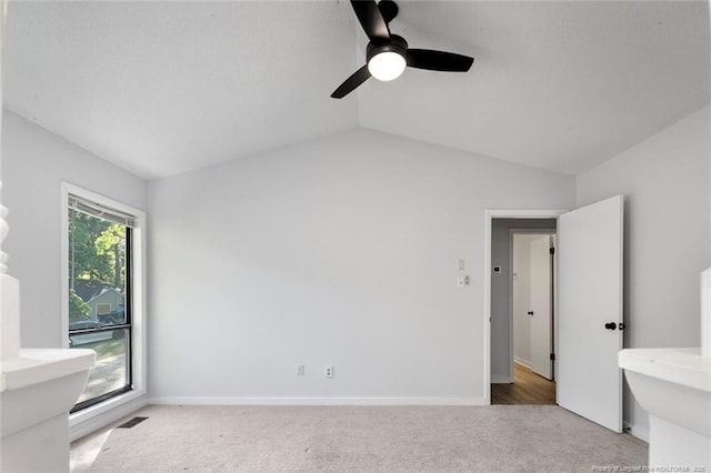 unfurnished bedroom with ceiling fan, visible vents, vaulted ceiling, baseboards, and light carpet