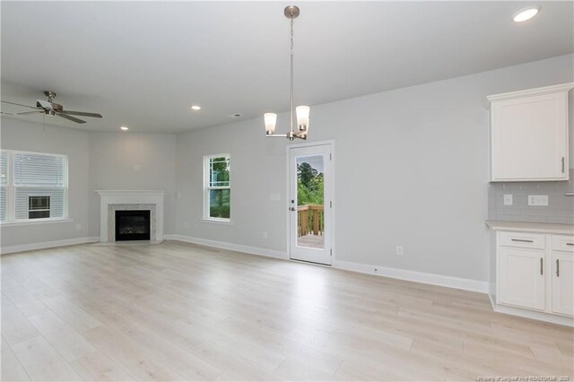 unfurnished living room featuring light wood-type flooring, recessed lighting, baseboards, and ceiling fan with notable chandelier