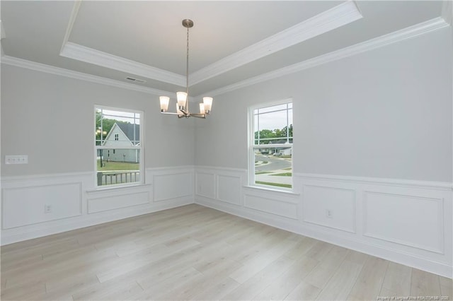 spare room with light wood finished floors, a raised ceiling, a chandelier, and wainscoting