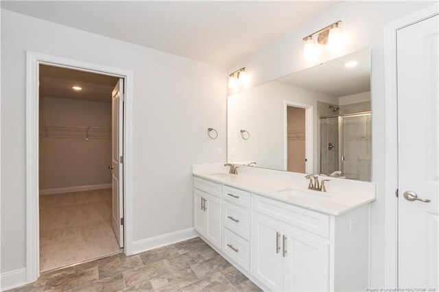 full bath featuring baseboards, a stall shower, double vanity, and a sink