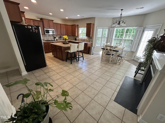 kitchen with appliances with stainless steel finishes, light countertops, light tile patterned floors, backsplash, and a kitchen breakfast bar