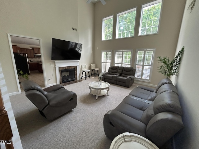 living area featuring a towering ceiling, carpet flooring, a premium fireplace, baseboards, and ceiling fan