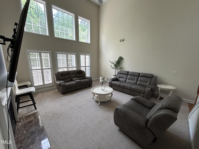 carpeted living room featuring healthy amount of natural light, a towering ceiling, baseboards, and ceiling fan